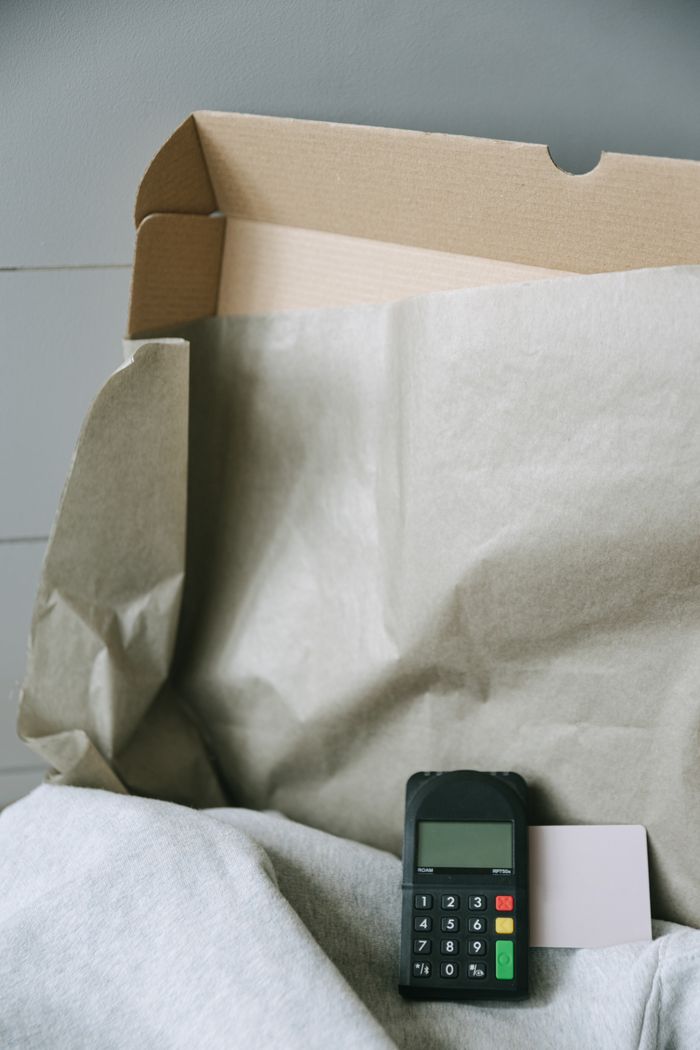 An image showing a payment terminal alongside a cardboard box and paper, illustrating online shopping and contactless payment.